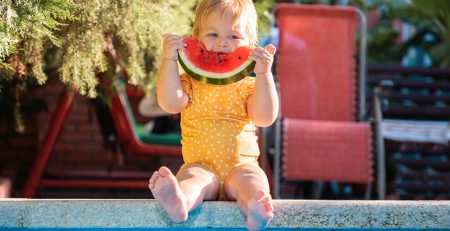 Baby eating watermelon by the pool