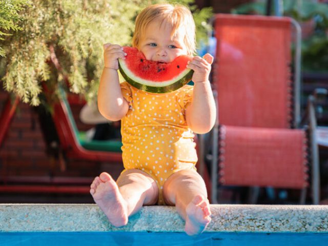 Baby eating watermelon by the pool